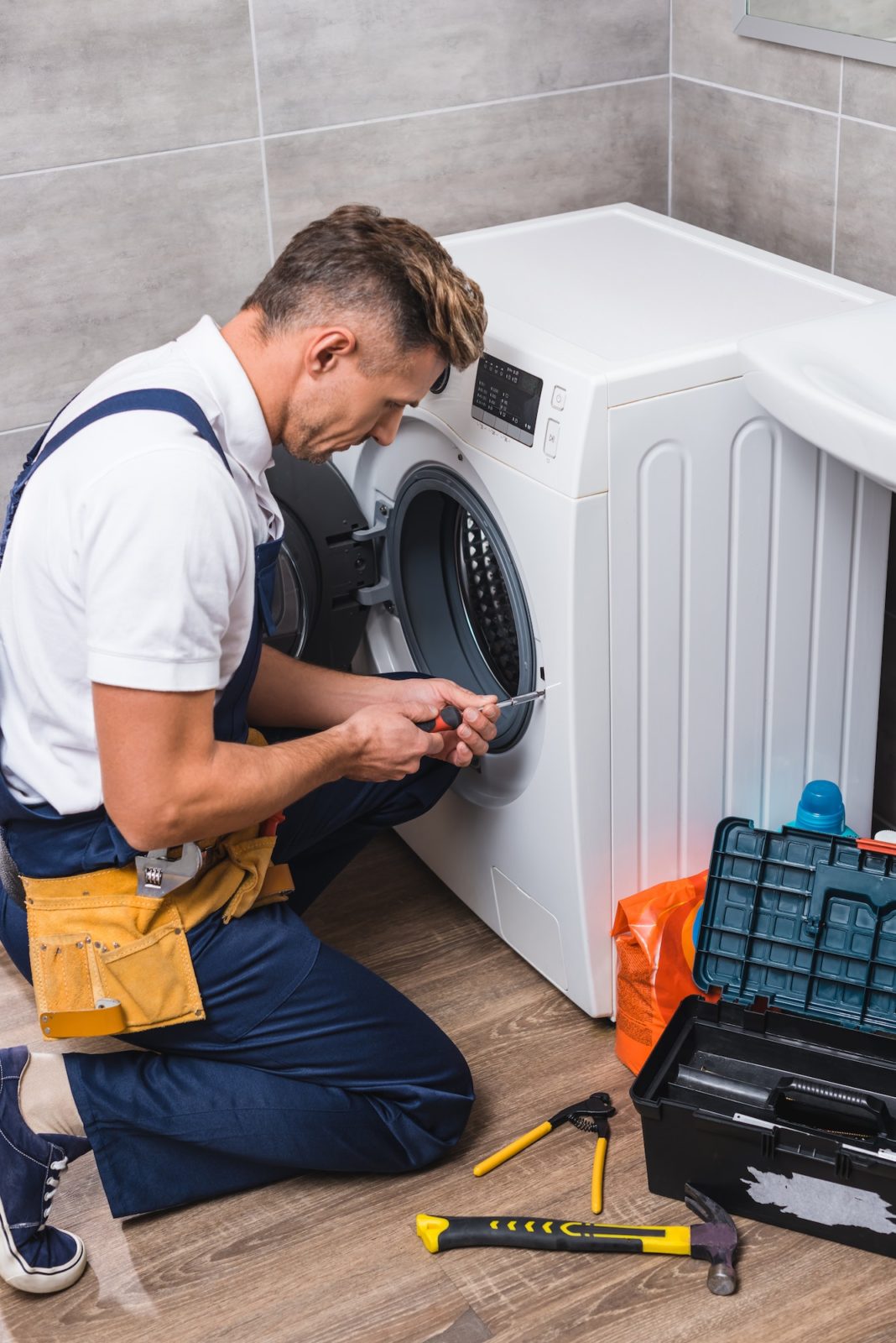 adult repairman working with screwdriver while repairing washing machine in bathroom